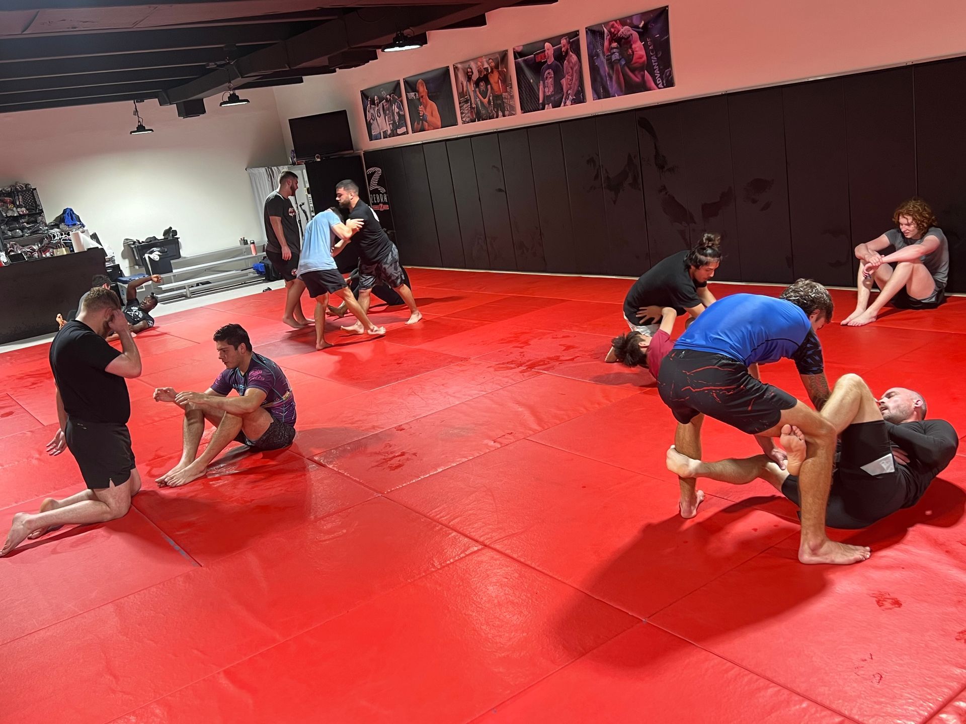 A group of people are practicing martial arts on a red mat in a gym.