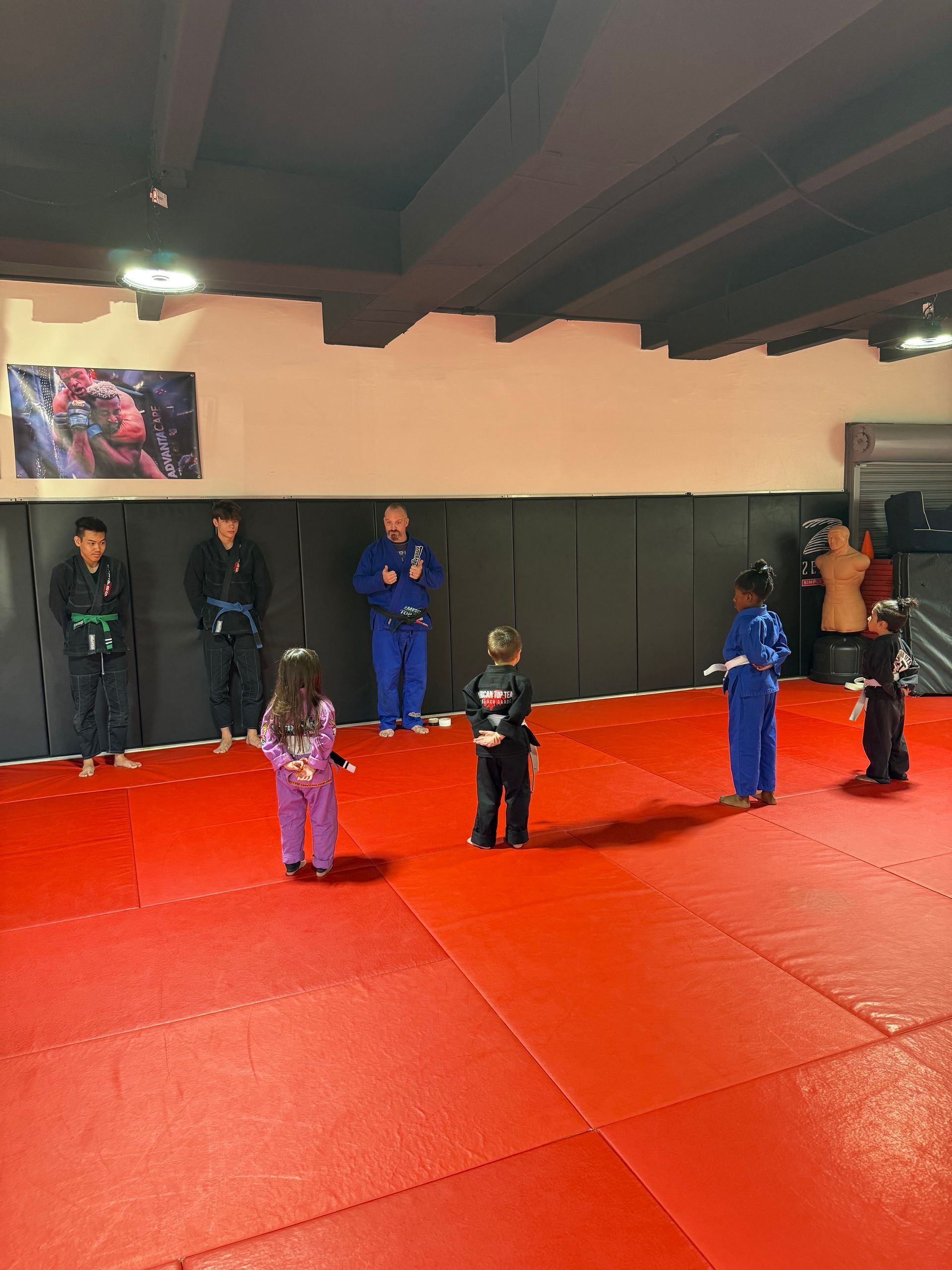 Three men are standing on a wrestling mat and one of them is wearing a yellow belt