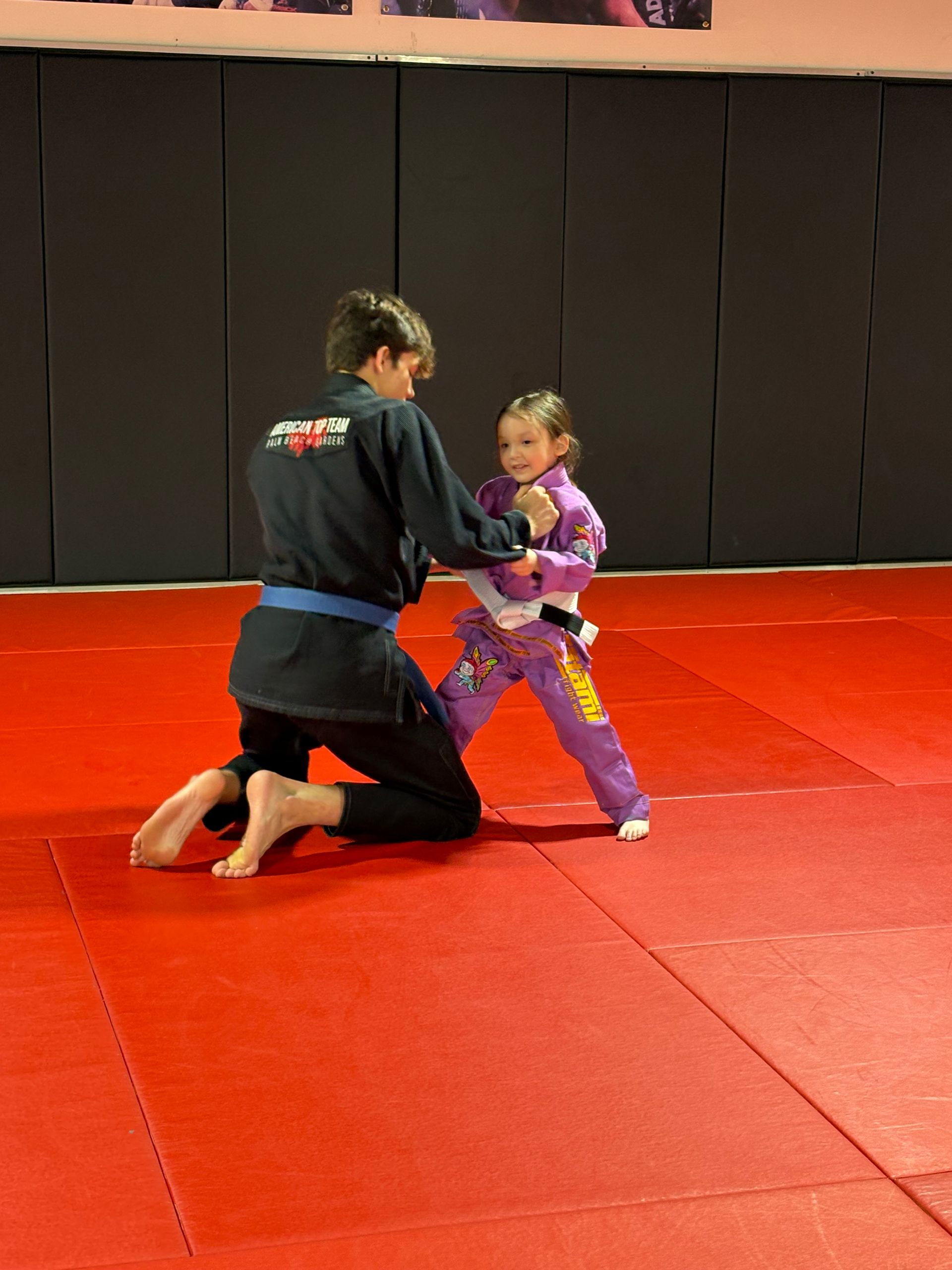 A woman is kneeling down next to a little girl on a red mat.