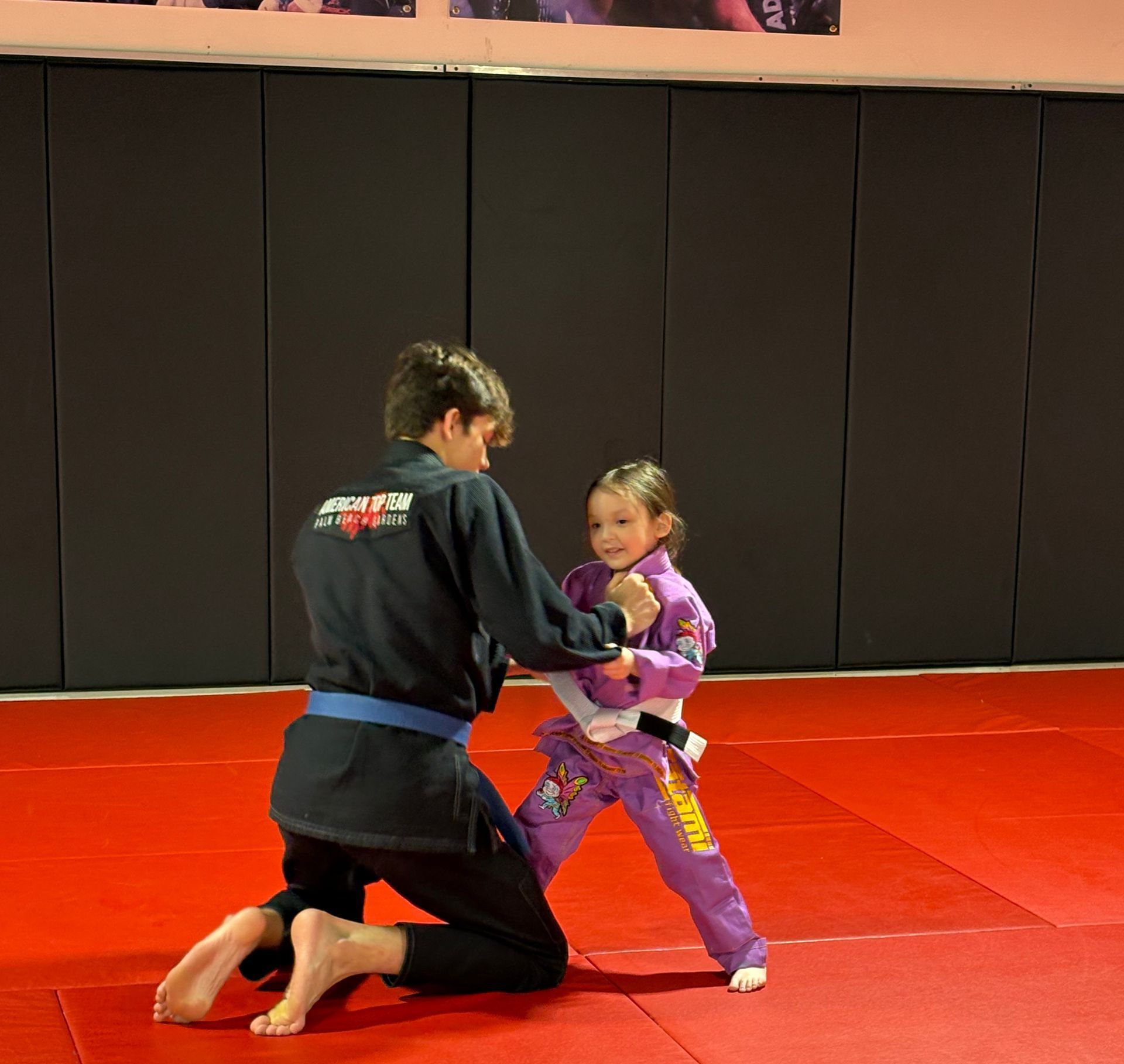 Three men are standing on a wrestling mat and one of them is wearing a yellow belt