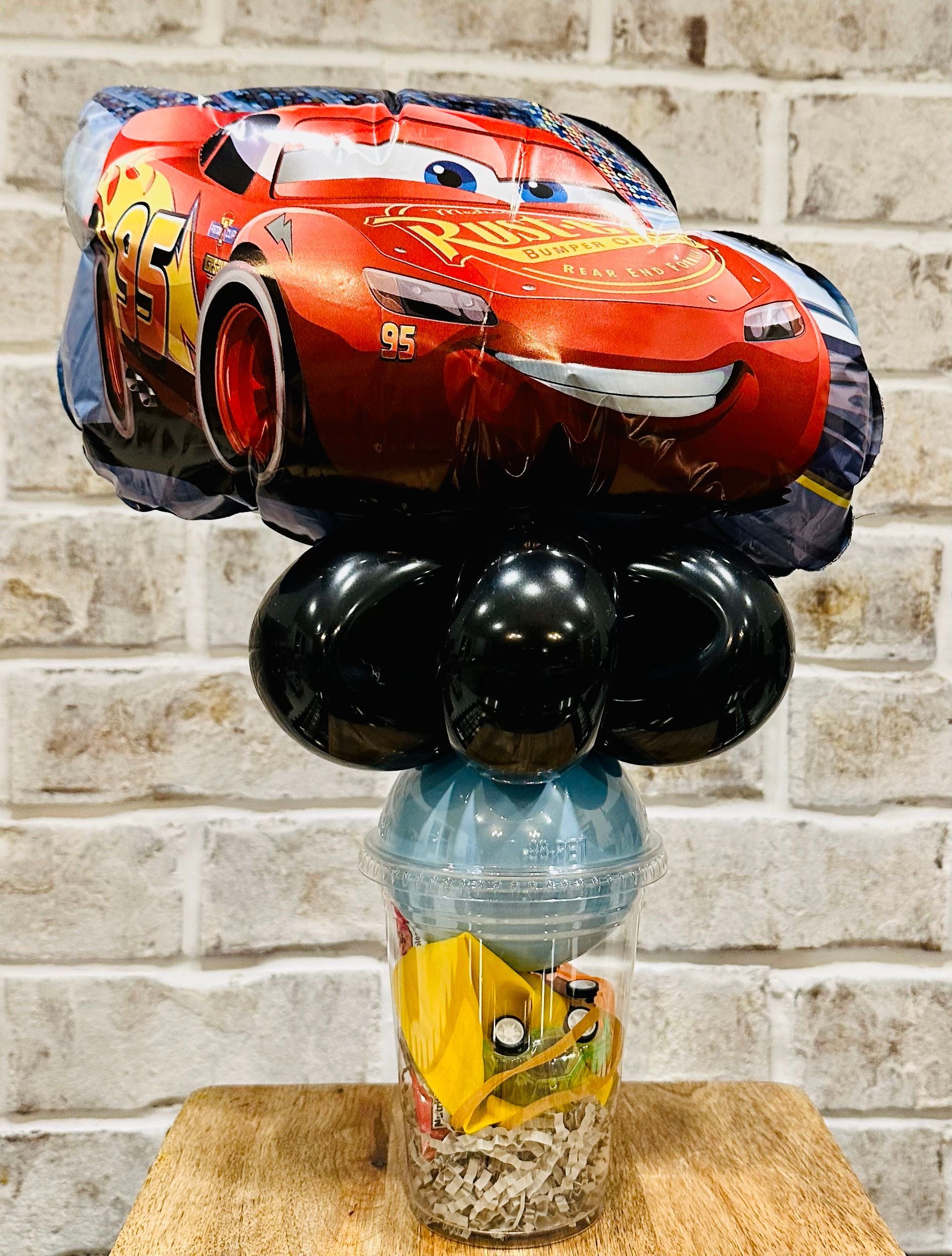 A lightning mcqueen balloon is sitting on top of a table with balloons.