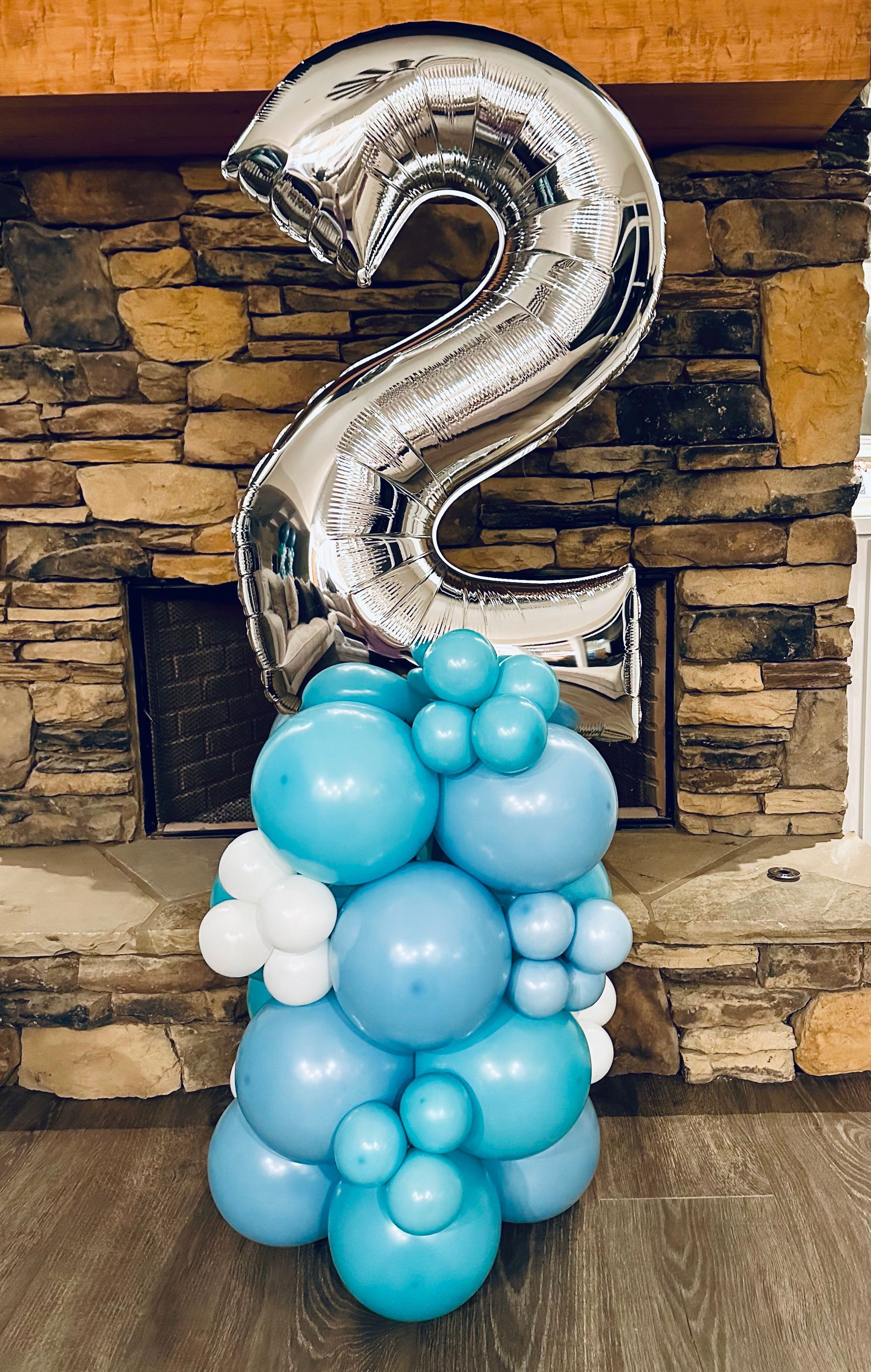 A silver number two balloon is sitting on top of a pile of blue and white balloons.