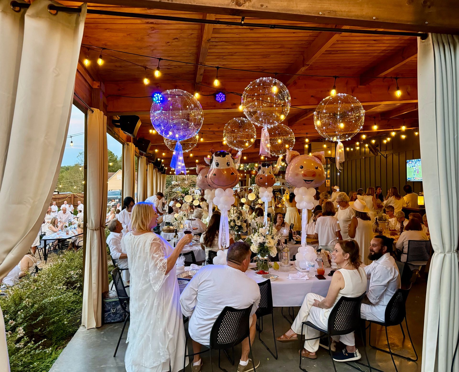 A group of people are sitting at tables in a room with balloons hanging from the ceiling.