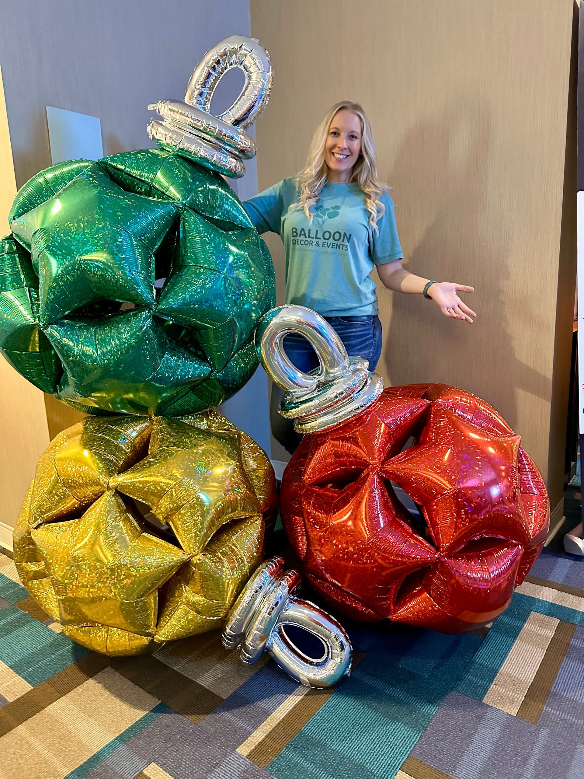 A woman is standing next to a stack of balloons that look like christmas ornaments.