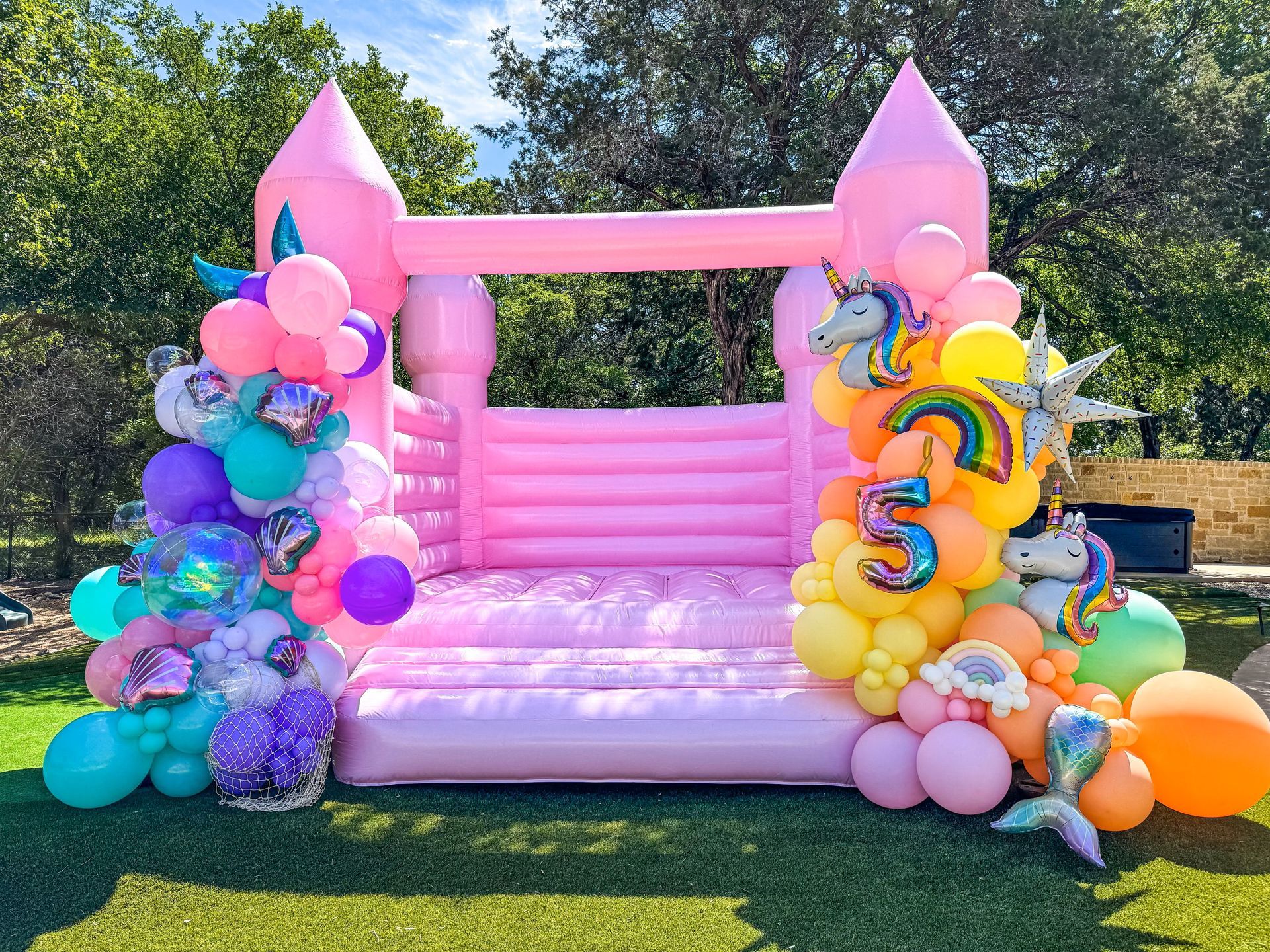 A pink bouncy castle decorated with balloons for a girl 's birthday.