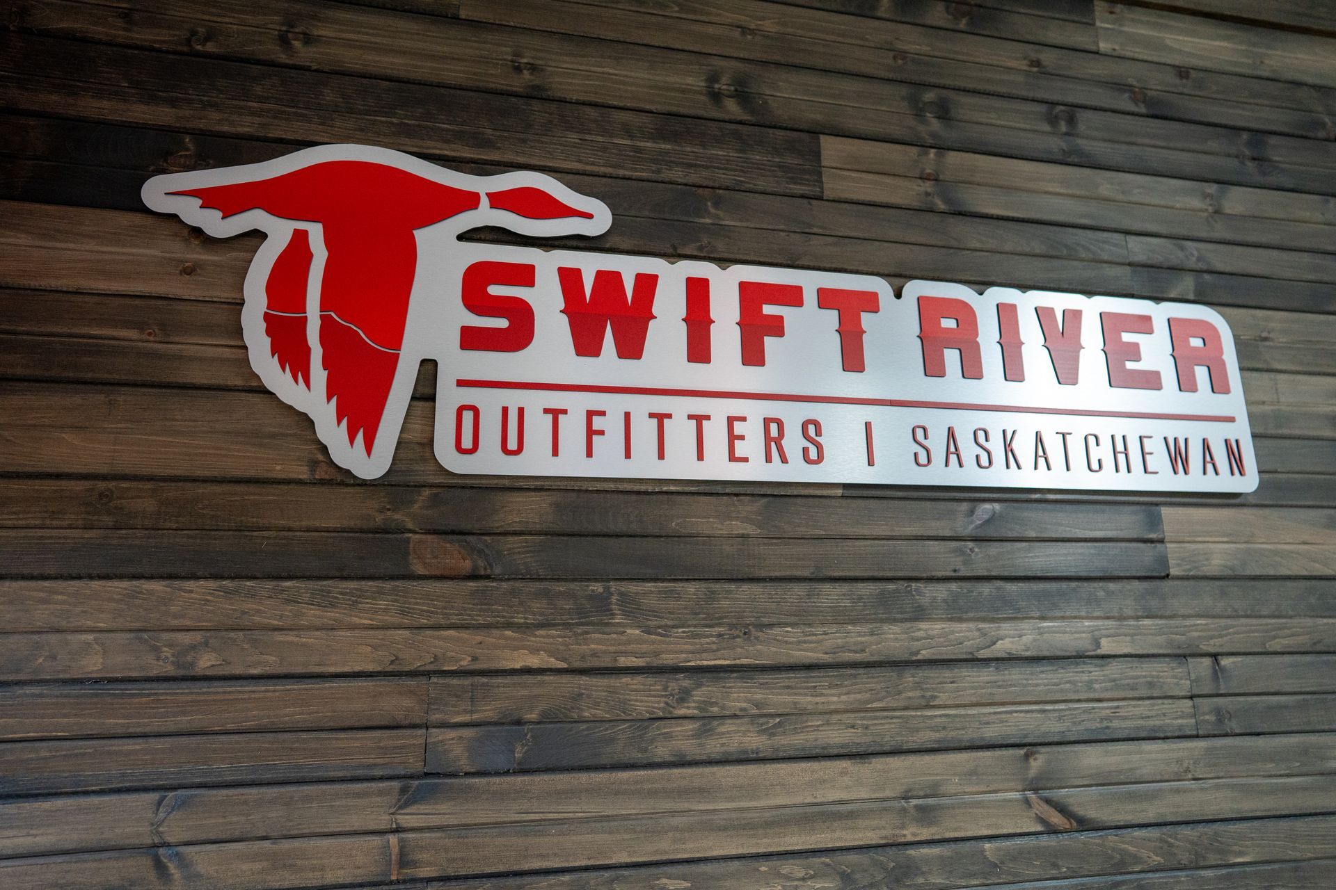 A sign for swift river outfitters is on a wooden wall