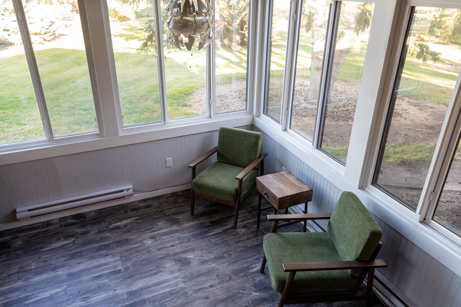 A sun room with two green chairs and a table.