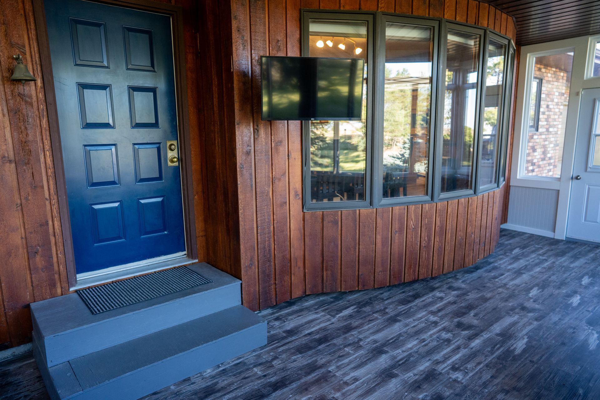 A porch with a blue door and a flat screen tv on the wall.