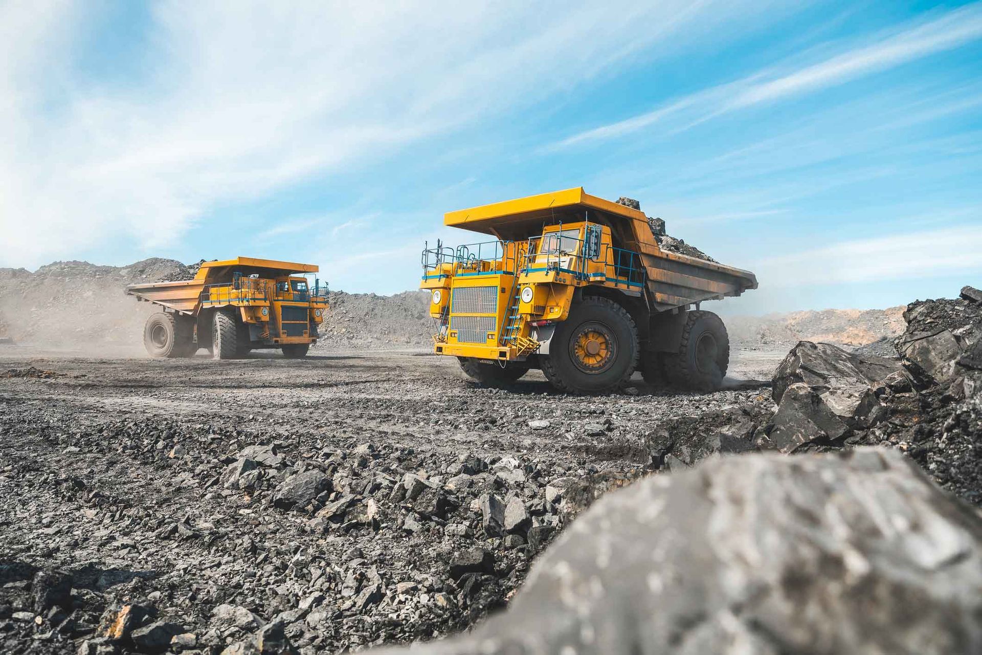 Two yellow dump trucks are driving through a rocky field.