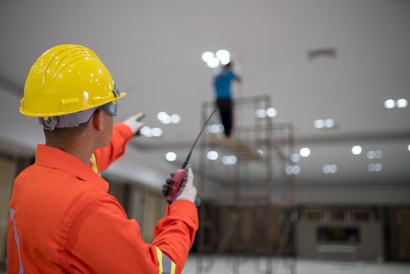 A Construction Worker Is Talking On A Walkie Talkie While A Man Is Standing On A Ladder – Brendale, QLD - DB Electrical
