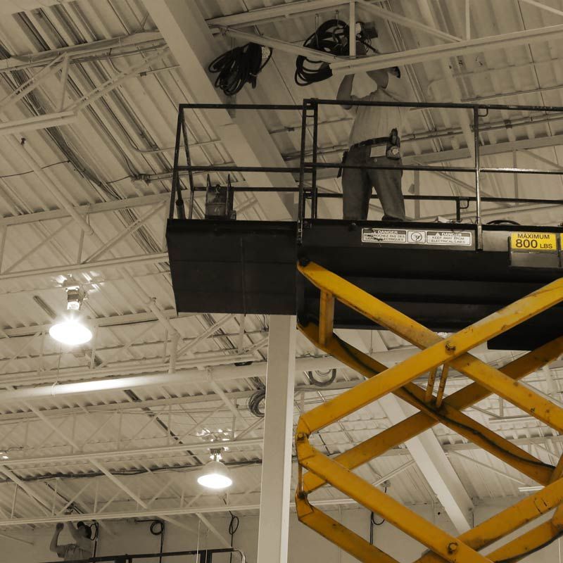 A Man Stands On A Scissor Lift With A Sign That Says 200 On It – Brendale, QLD - DB Electrical