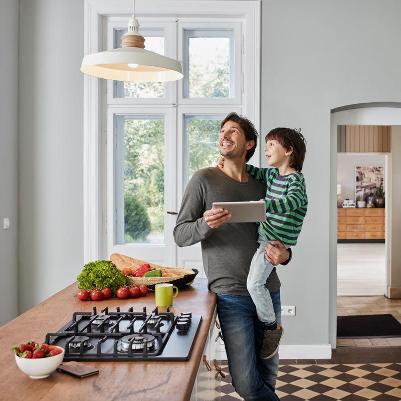 A Man Is Holding A Child While Looking At A Tablet In A Kitchen – Brendale, QLD - DB Electrical