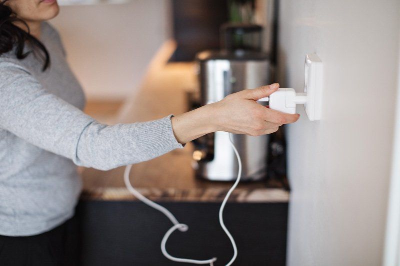A Woman Is Plugging A Plug Into A Wall Socket – Brendale, QLD - DB Electrical