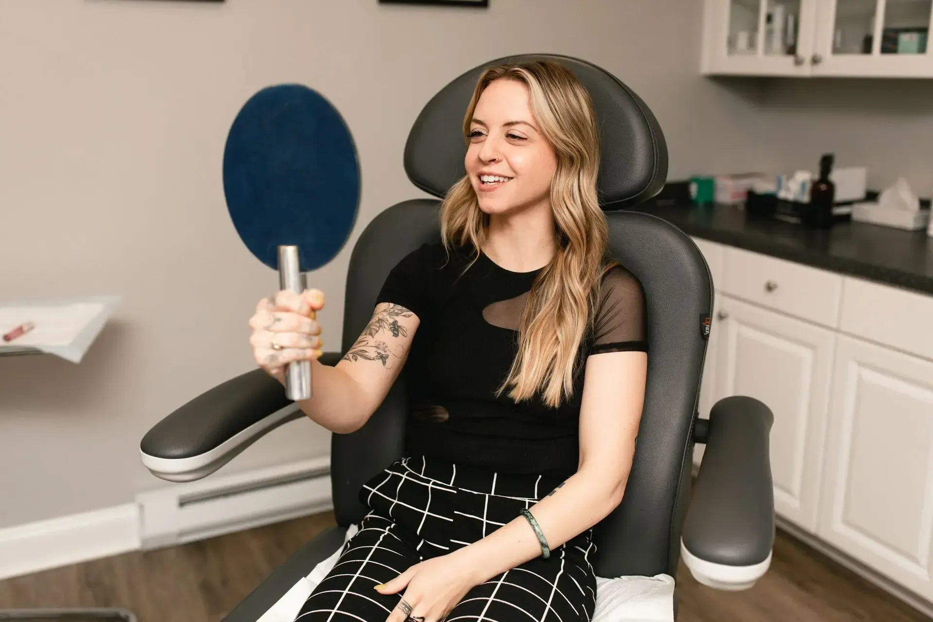 A woman is sitting in a chair holding a mirror.