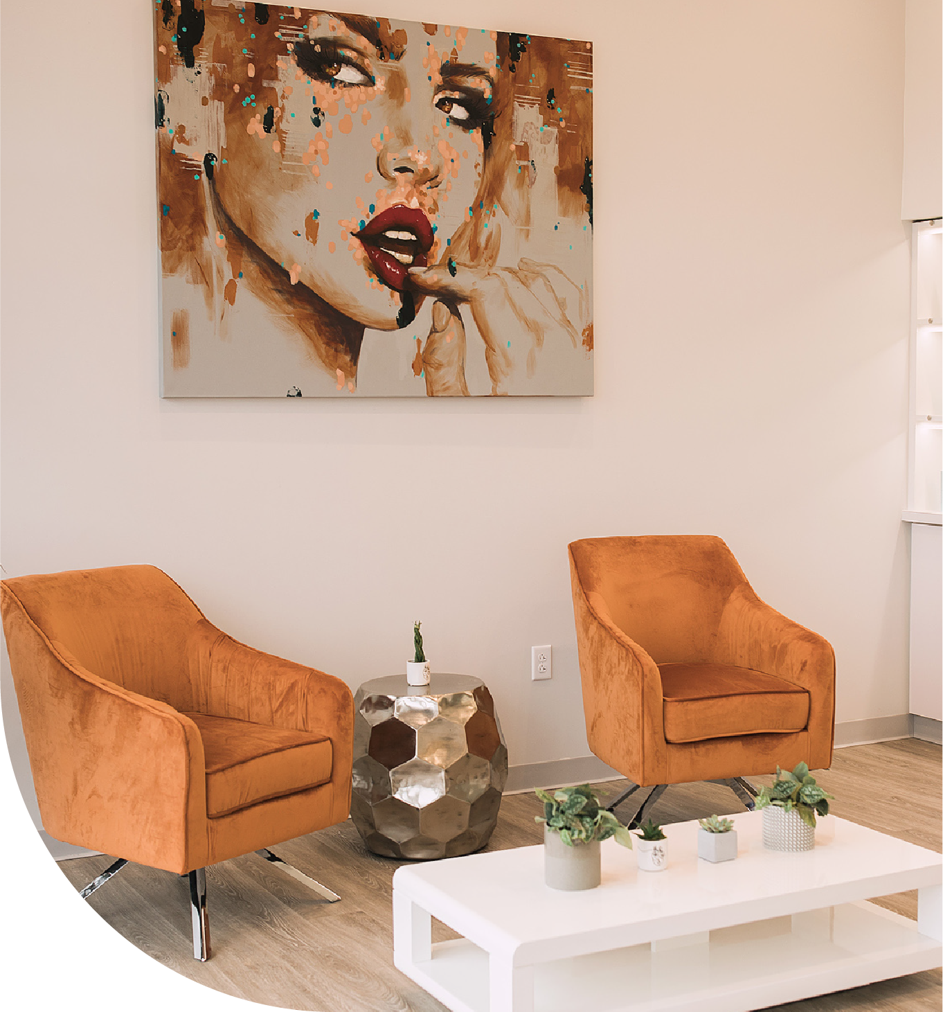 A painting of a woman 's face hangs above two chairs and a coffee table