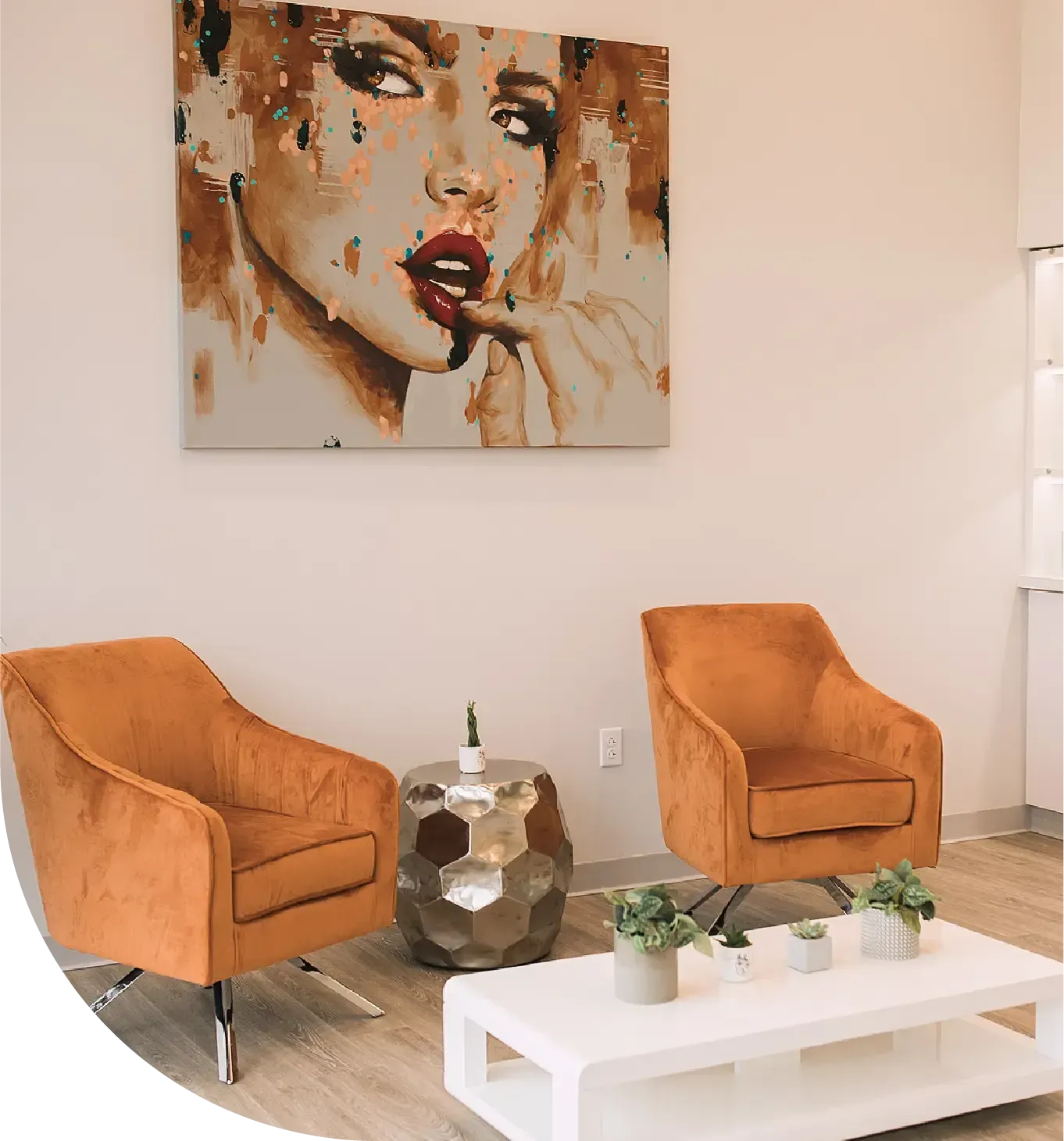 A painting of a woman 's face hangs above two chairs and a coffee table