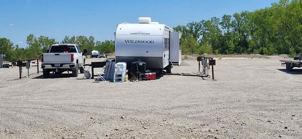 White travel trailer and pickup truck parked on a gravel campsite with trees in the background