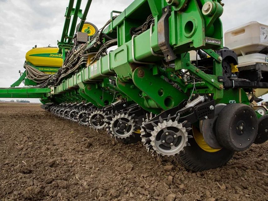 A green and yellow tractor is plowing a field.