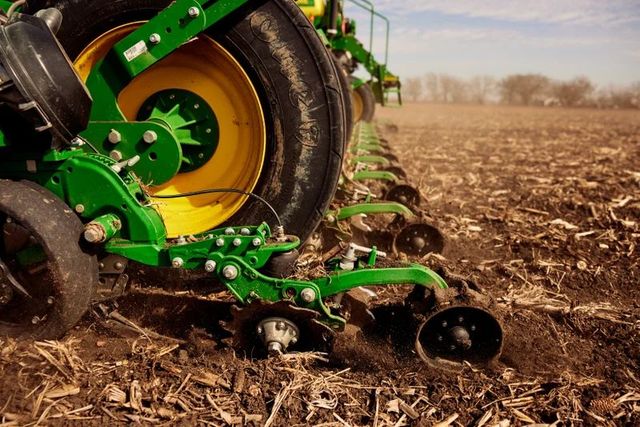 A green and yellow tractor is plowing a field.