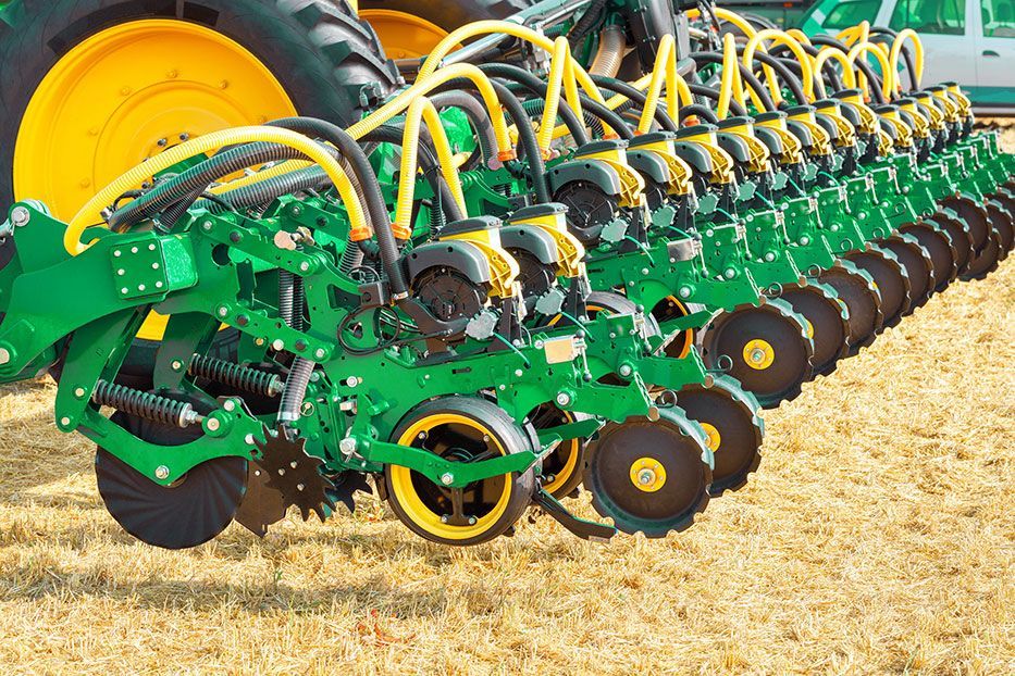 A green tractor is plowing a field with a green plow attached to it.