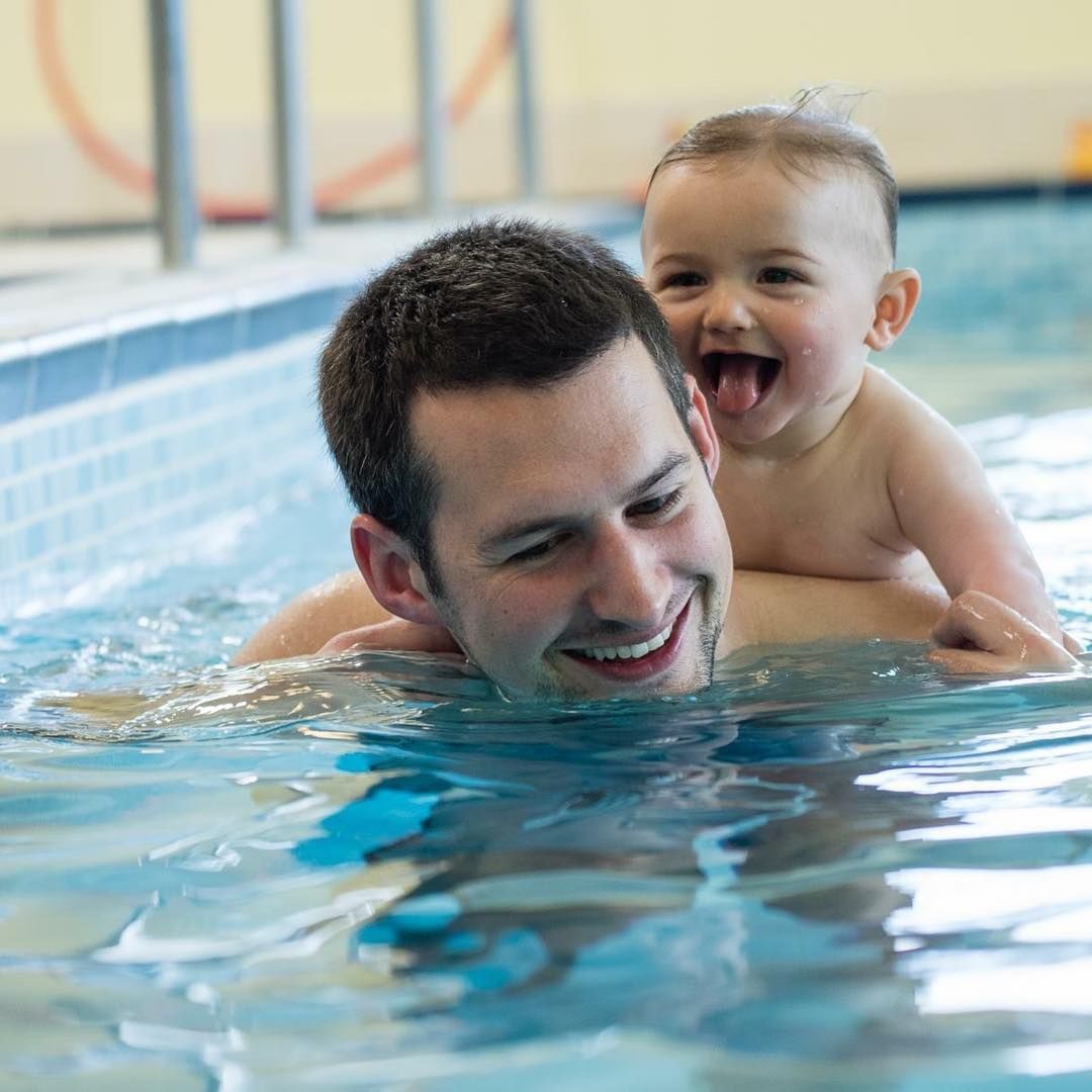 Man Swimming in Pool, Carrying Smiling Baby on His Back — Swim Care Boambee in Coffs Harbour, NSW