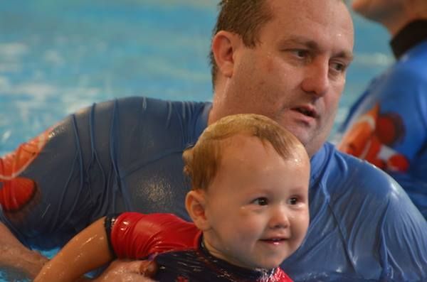 Man in Blue Shirt Holding Smiling Baby in Pool โ Swim Care Boambee in Coffs Harbour, NSW