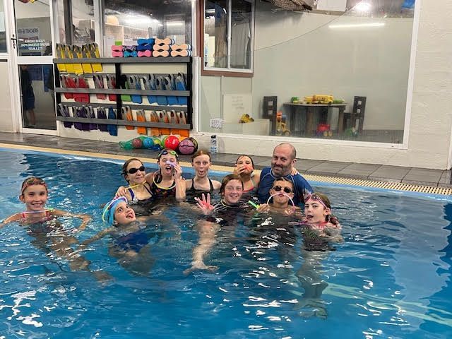 Group of children and a man smiling in a swimming pool โ Swim Care Boambee in Coffs Harbour, NSW