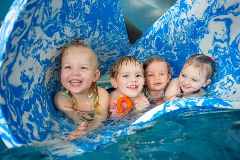 Four Young Children in A Pool, Lying on A Flotation Device โ Swim Care Boambee in Boambee, NSW