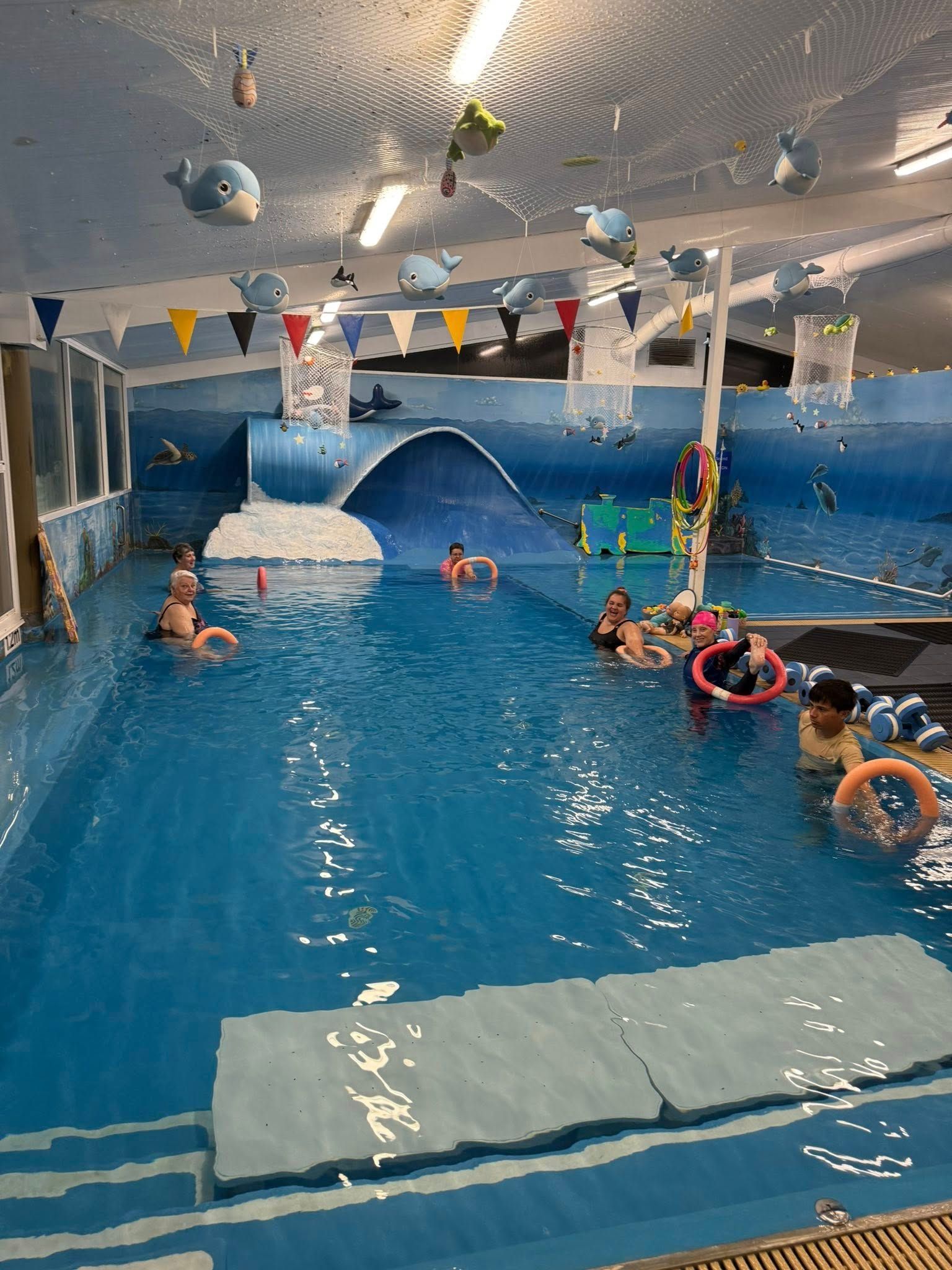 A group of ladies and men are in a swimming pool while holding floaties โ Swim Care Boambee in Coffs Harbour, NSW