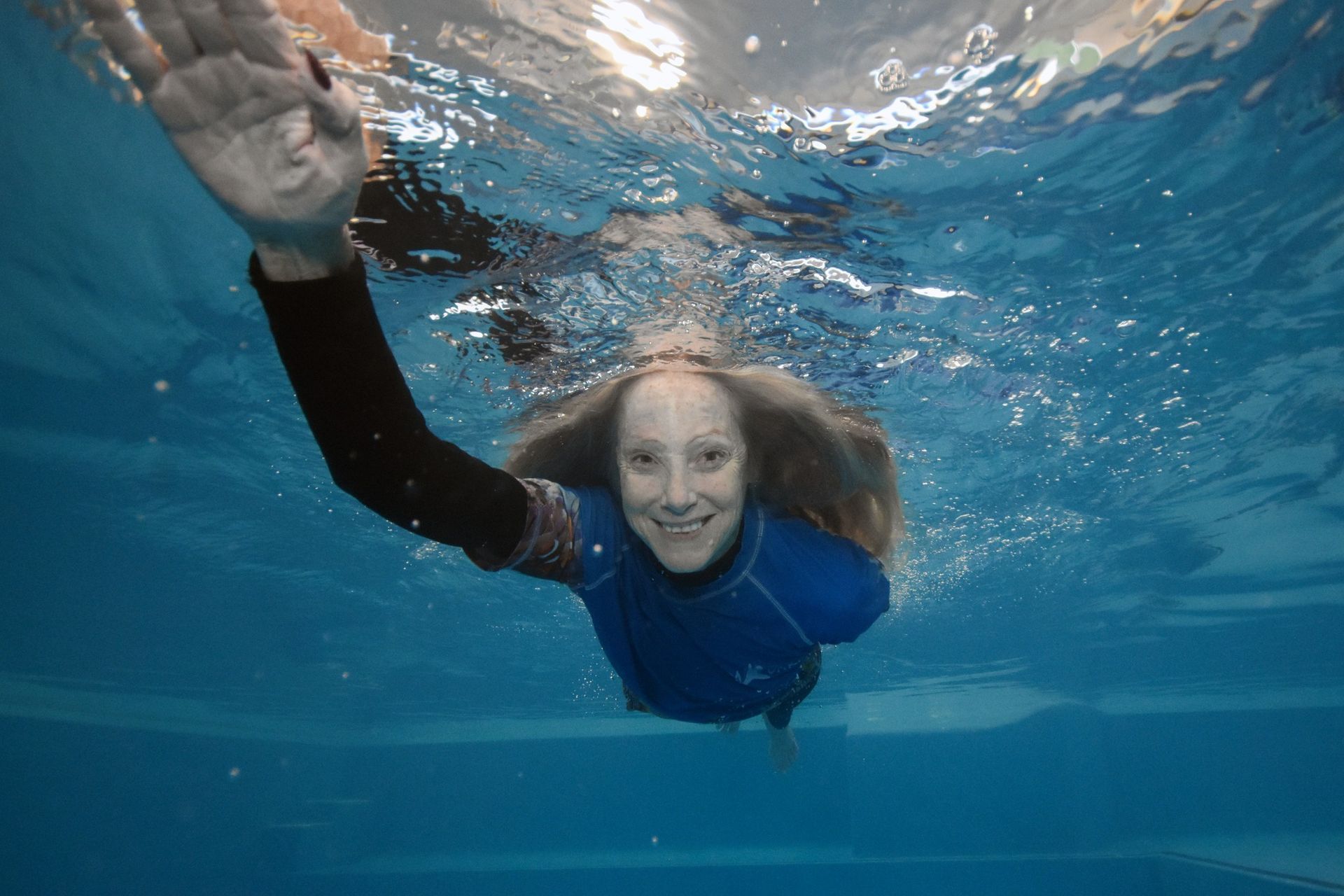 Senior Woman Swimming Underwater In Blue Pool Water
