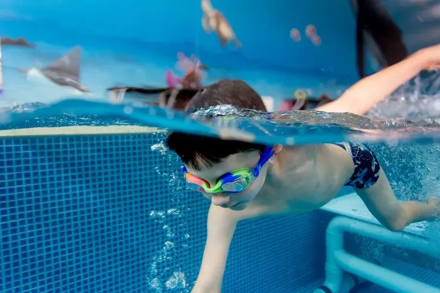 Boy in Swim Goggles Underwater, Swimming in A Blue-Tiled Pool — Swim Care Boambee in Coffs Harbour, NSW