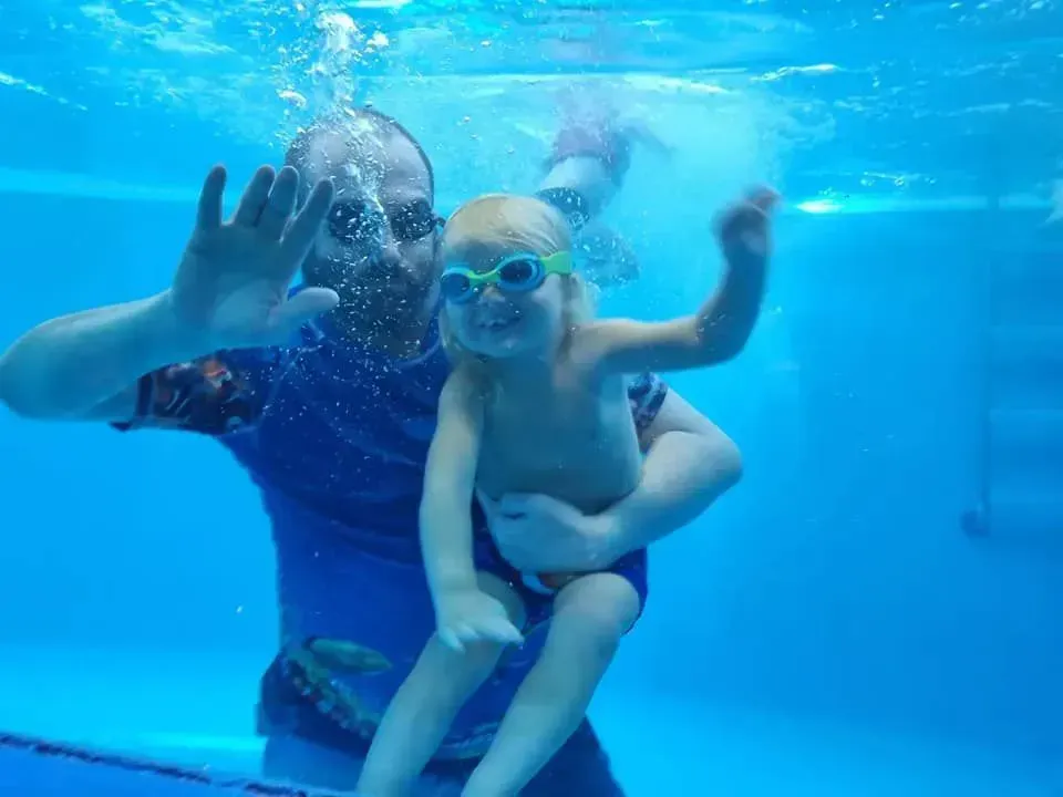 Man Holding Child Underwater, Both Wearing Goggles, Smiling, in A Pool — Swim Care Boambee in Coffs Harbour, NSW