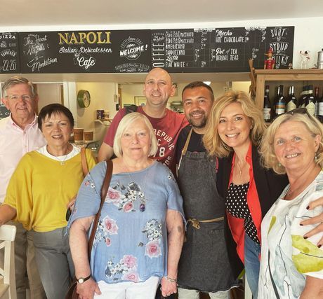 Group of smiling people posing inside a café with a Napoli sign and chalkboard menu in the background
