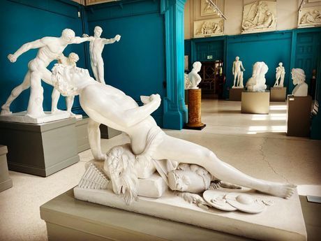 White classical statues in a teal museum gallery, including a dramatic fallen figure in the foreground.