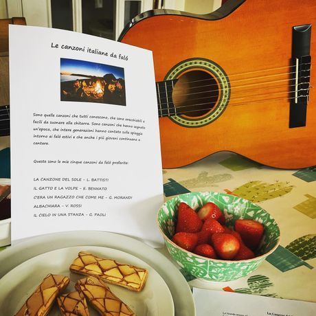 Cookbook page beside an orange guitar, with a plate of pastries and a bowl of strawberries on a table