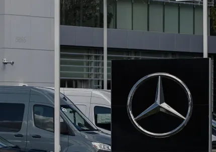 Mercedes logo on a black sign outside a modern building, with parked vans in front.