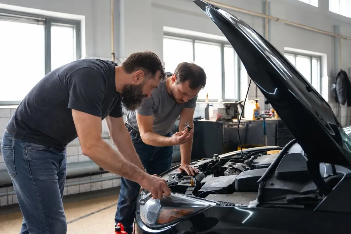 Two mechanics inspect a black car with its hood open in a garage
