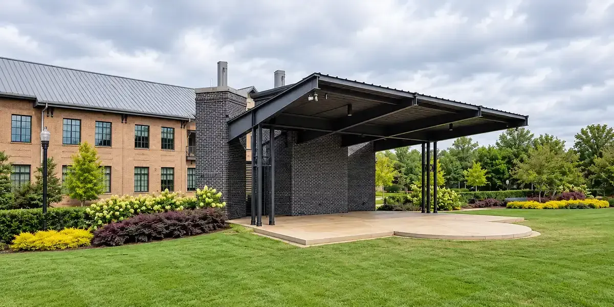 Modern brick building with a covered stage pavilion and landscaped lawn and flowers