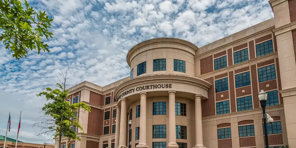 Grand courthouse building with columns, tan stone, red brick, and a curved entrance under a blue sky