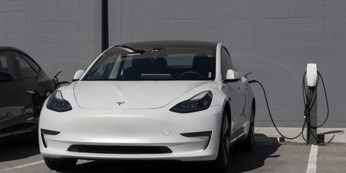 White Tesla Model 3 plugged into a charging station in a parking lot