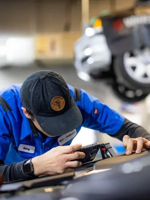 Mechanic in blue uniform inspecting a car with a diagnostic tool in a garage
