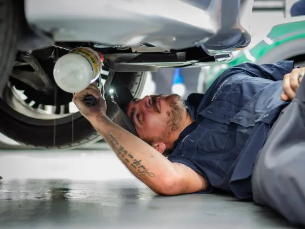 Mechanic lying under a car, inspecting the underside with a flashlight in a wet garage