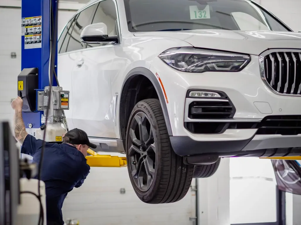 White SUV lifted in a garage while a mechanic works underneath on a car lift