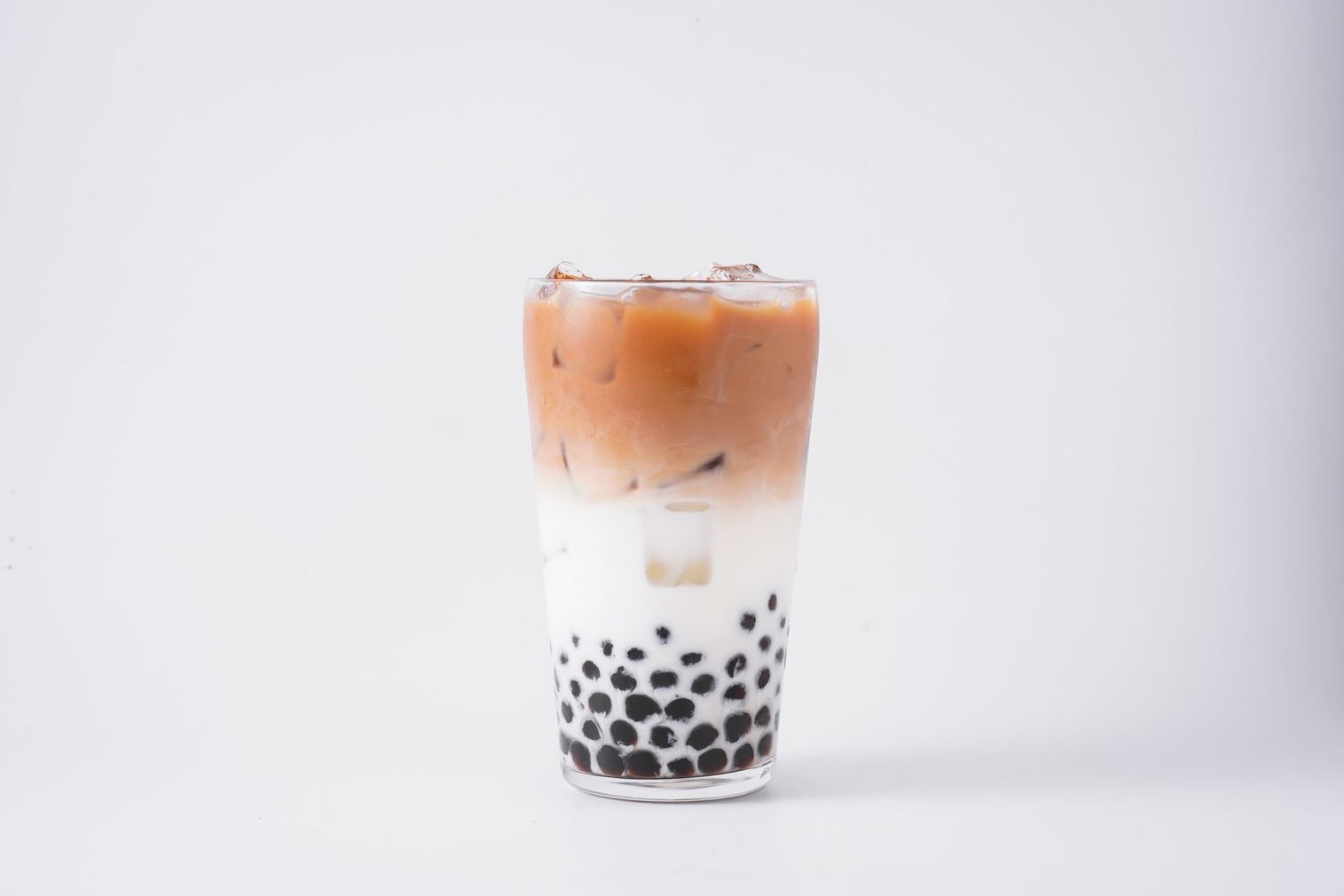 Iced bubble tea in a clear glass with layered milk, tea, ice, and black tapioca pearls