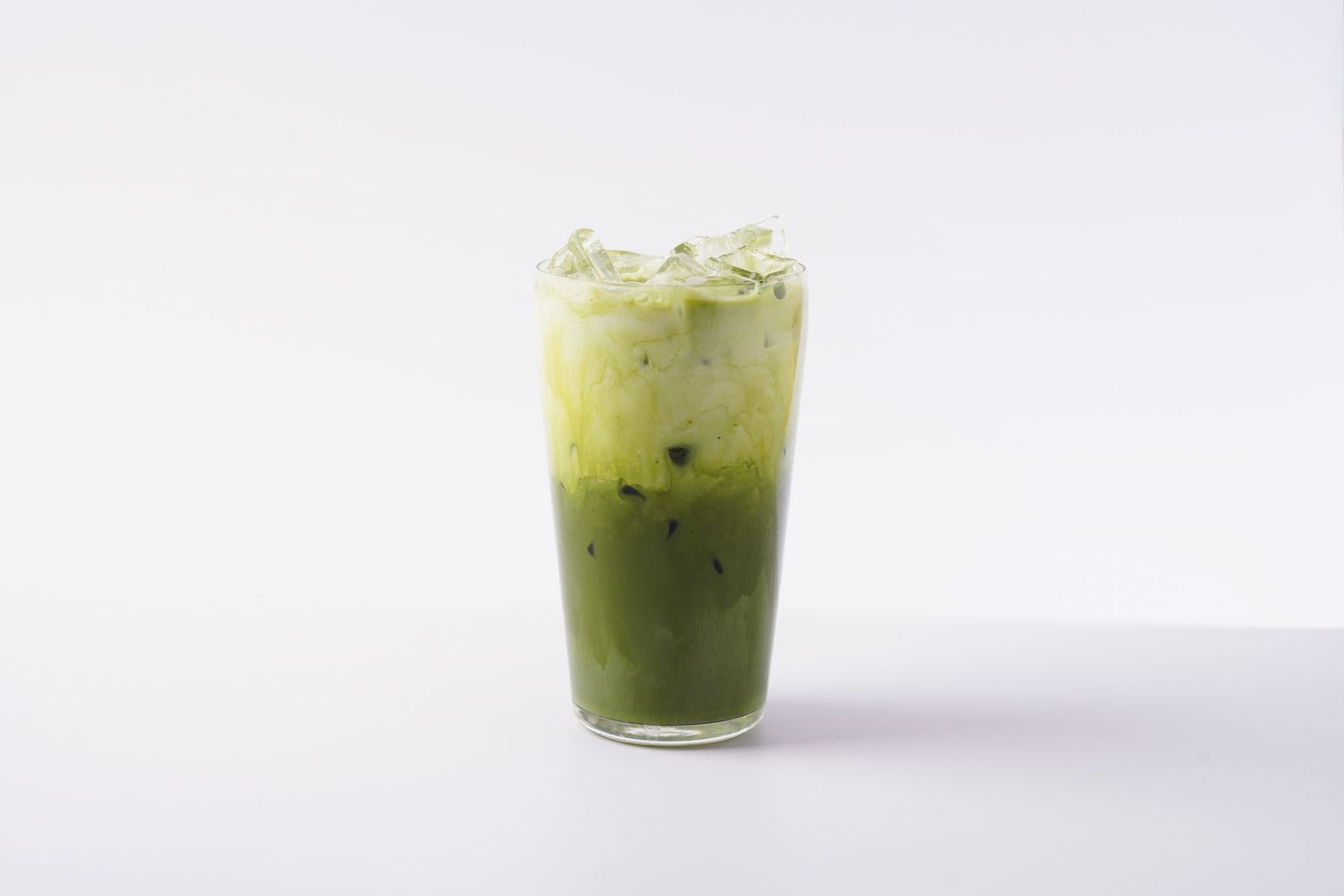 Tall green iced drink with whipped topping in a clear glass on a white background