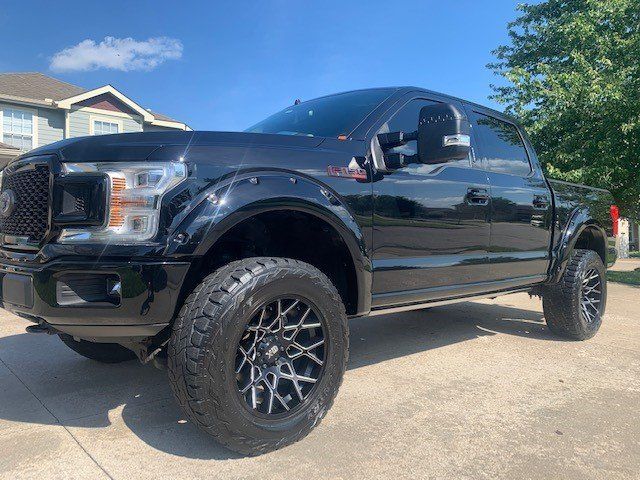 A black ford f150 truck is parked in a driveway in front of a house.
