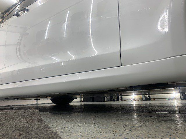 A white car is parked on a concrete floor in a garage.