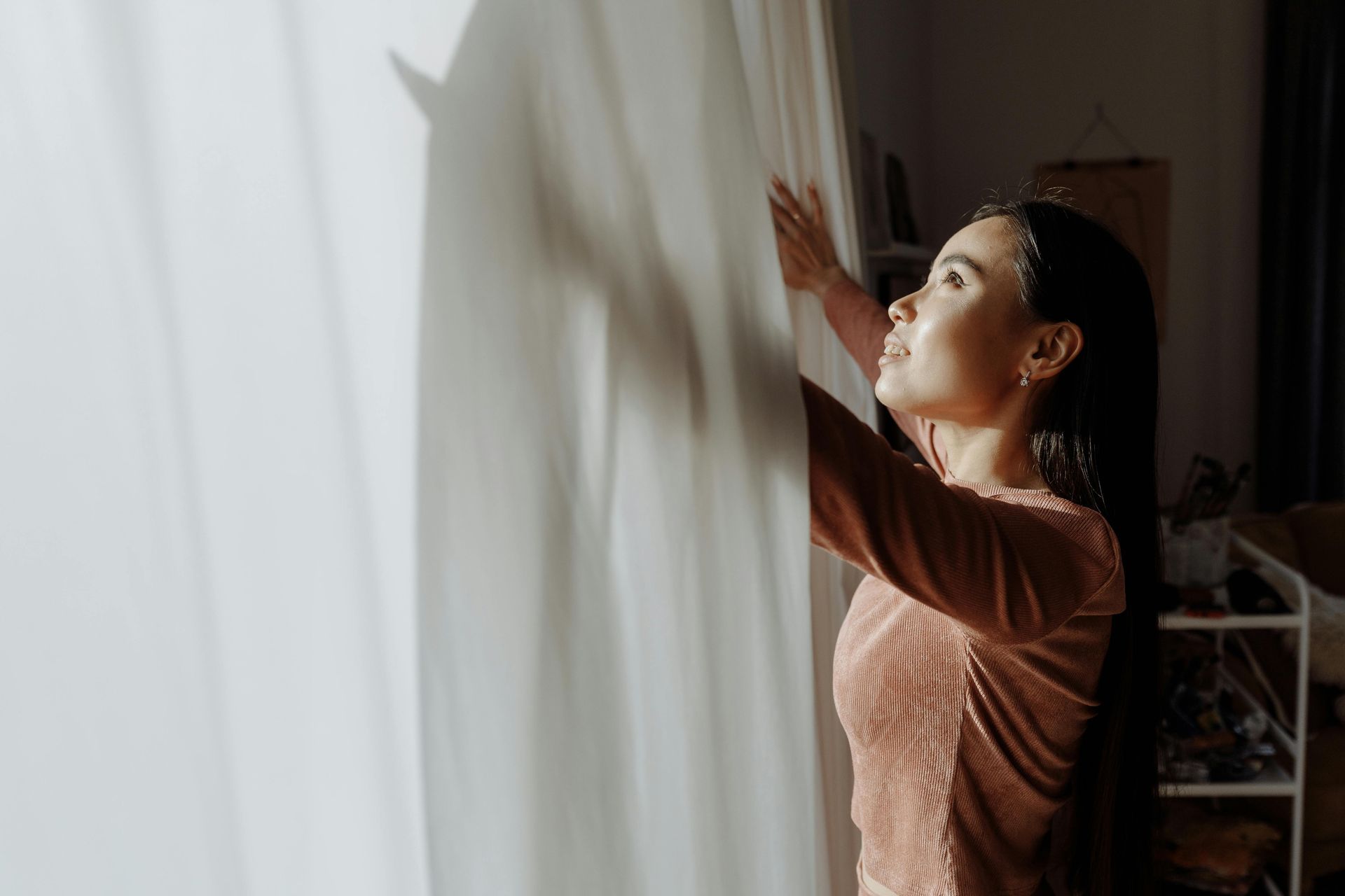 Woman adjusting sheer curtains in a sunlit room