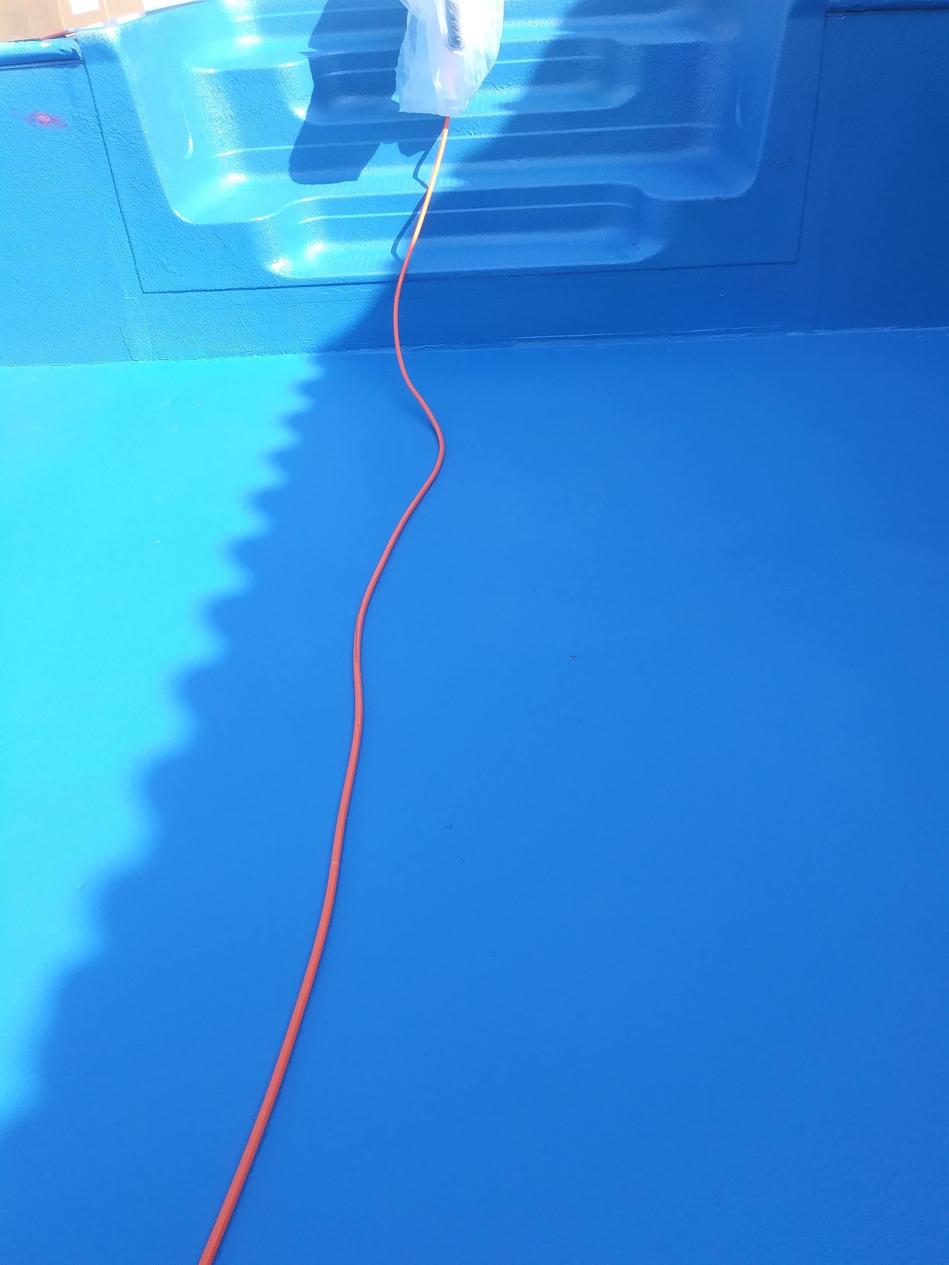 Blue swimming pool with a red rope hanging into the water from the edge