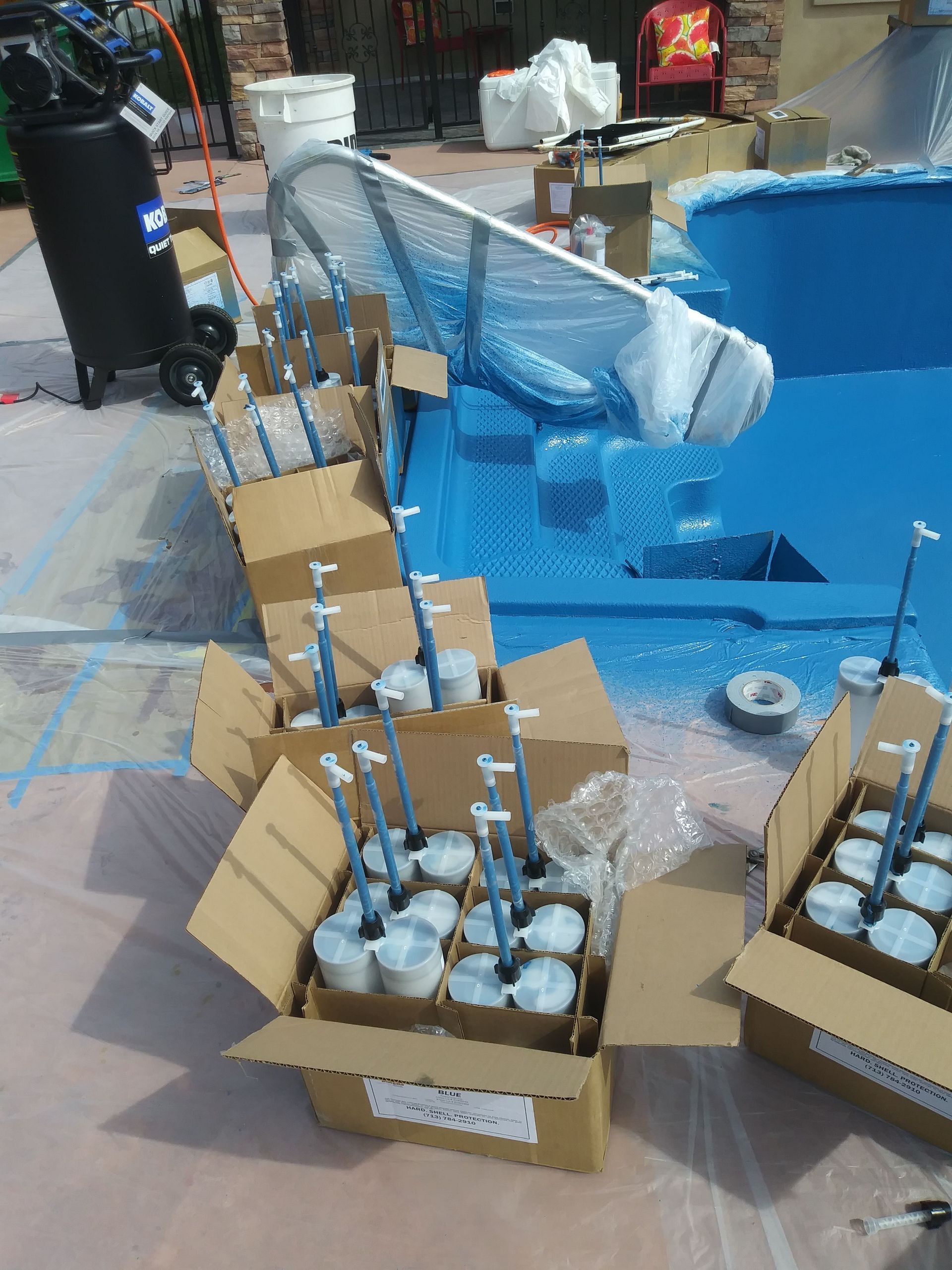 Boxes of white bulbs and metal poles arranged on a blue tarp in an outdoor work area